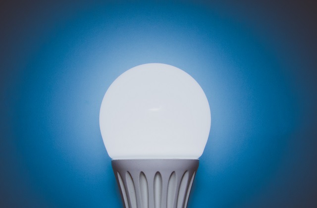 White energy-efficient bulb glowing. Blue background.